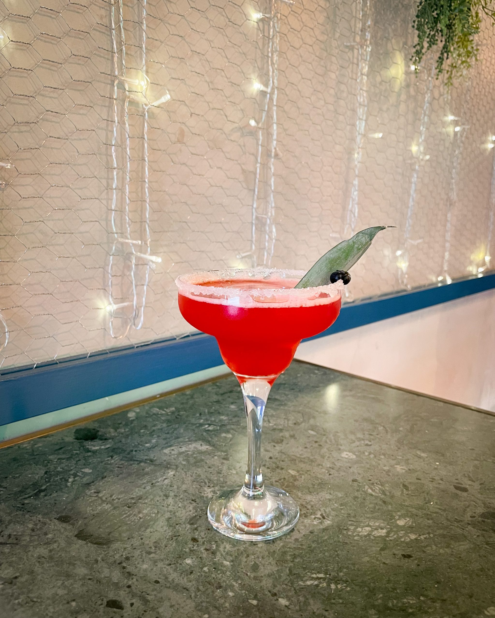 Coctel rojo servido en una copa junto a una ventana.